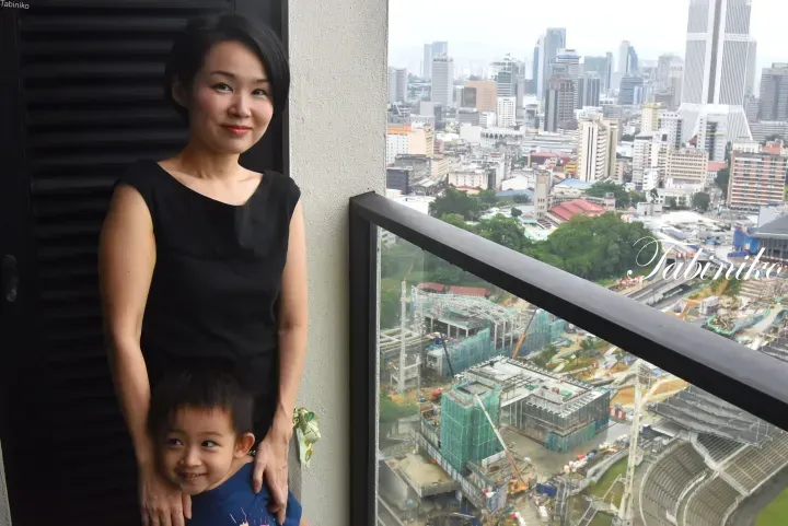 A woman and young boy stand on a balcony overlooking a city skyline and a large construction site.