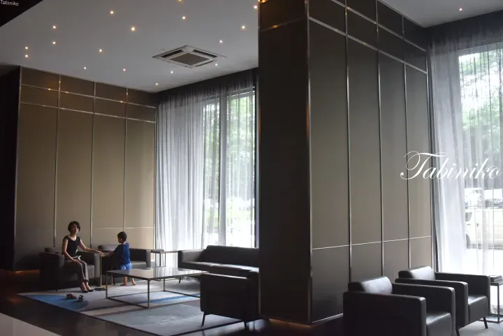 Modern hotel lobby with sleek furniture, floor-to-ceiling windows, and guests relaxing in a bright, contemporary space.
