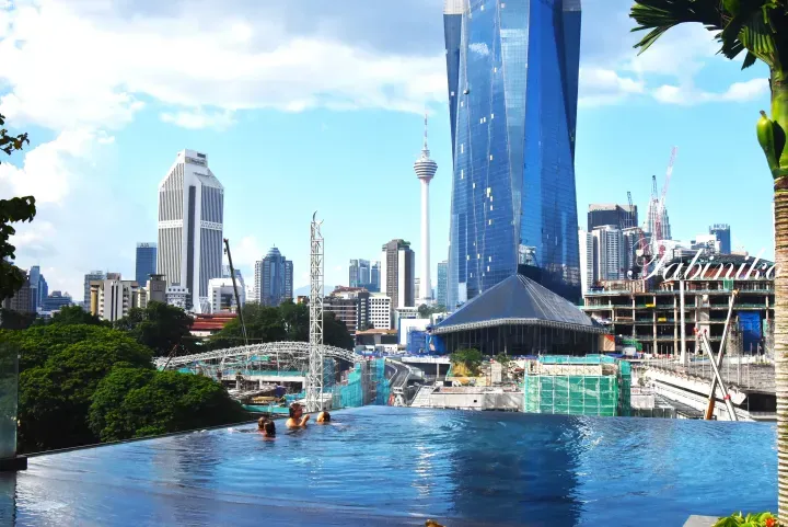 Swimmers at an infinity pool overlooking the Kuala Lumpur skyline, featuring Merdeka 118 and the KL Tower.