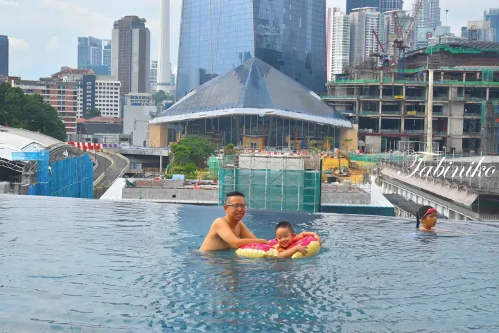 A family enjoys the infinity pool at The Exchange TRX with the iconic glass pyramid and Kuala Lumpur skyline in the background.