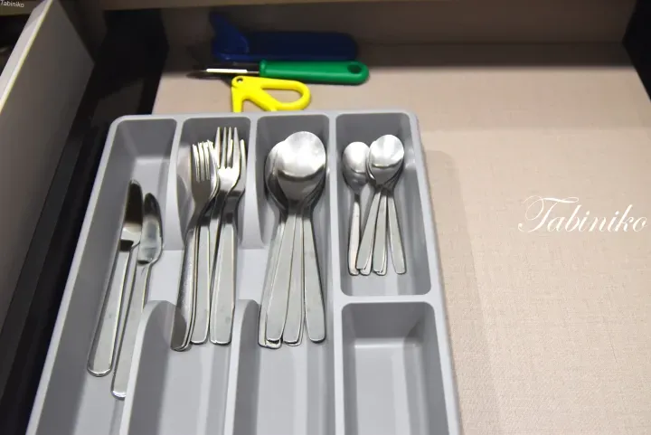 Organized silverware in a grey drawer tray, featuring knives, forks, and spoons neatly arranged in compartments.