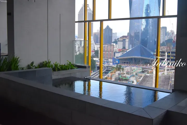 Infinity pool overlooking Kuala Lumpur skyline with Menara Maxis and Merdeka 118 visible through yellow window frames.