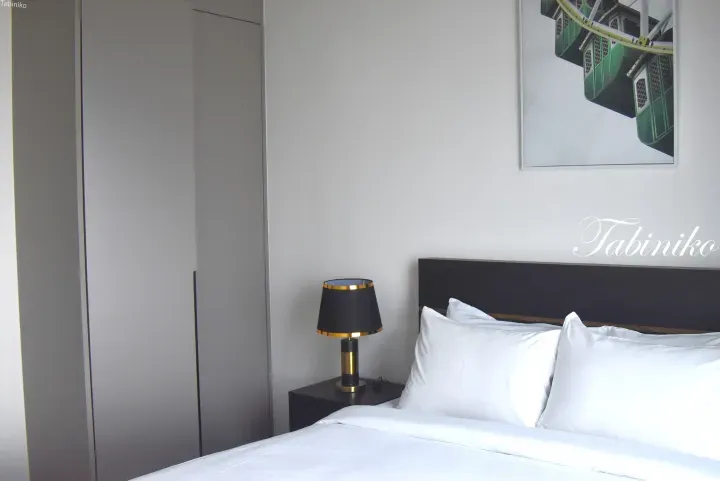 Modern hotel bedroom with white linens, a black lamp, and a green Ferris wheel artwork.