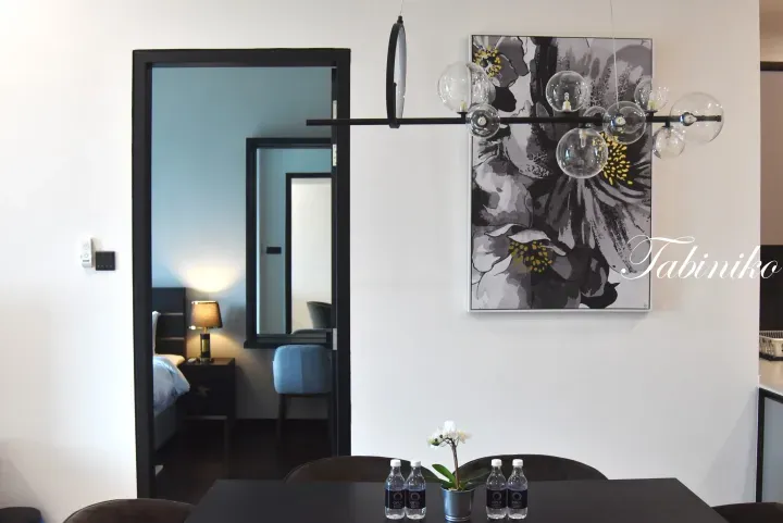 Modern dining area with black table, glass pendant lights, floral artwork, and view into a bedroom with blue accents.
