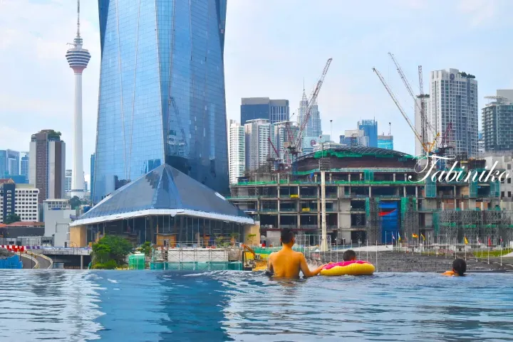 Guests relax in the infinity pool overlooking the Kuala Lumpur skyline, featuring the Menara KL and Merdeka 118.