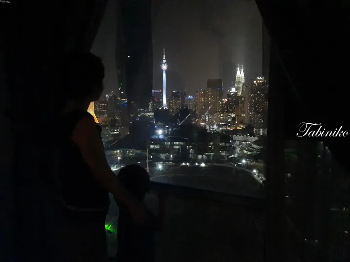 KLタワーとペトロナスツインタワーズが光るクアラルンプールの夜景を眺める人物と子供のシルエット。