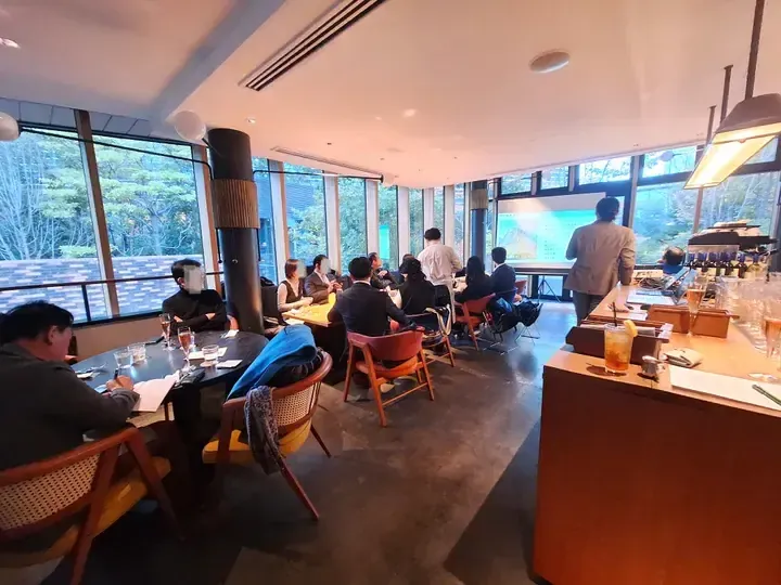 Attendees at a property presentation in a bright cafe with large windows overlooking a green landscape.