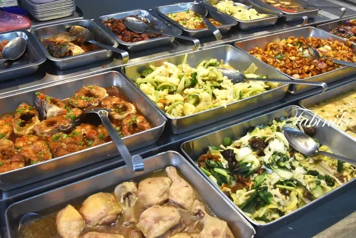 Variety of Chinese dishes served in stainless steel trays at a buffet, including braised fish, chicken, and mixed vegetables.