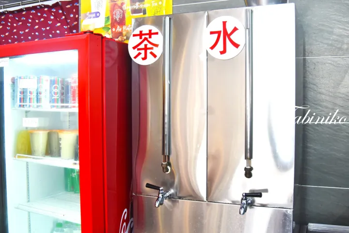 「茶」と「水」の表示があるステンレス製飲料サーバーと、隣に並ぶ赤い飲料冷蔵庫。