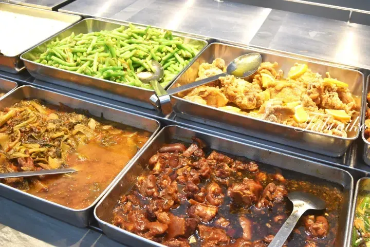 Buffet trays with stir-fried green beans, lemon chicken, braised vegetables, and braised pork trotters at a Malaysian food stall.