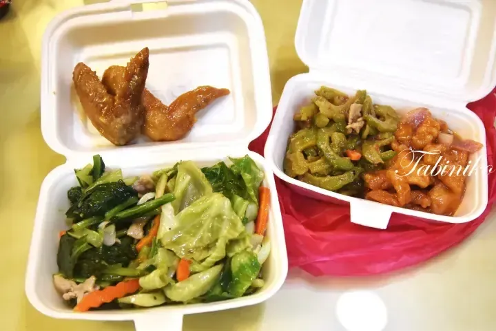 Styrofoam takeaway containers with braised chicken wings, stir-fried vegetables, bitter gourd, and sweet and sour pork.