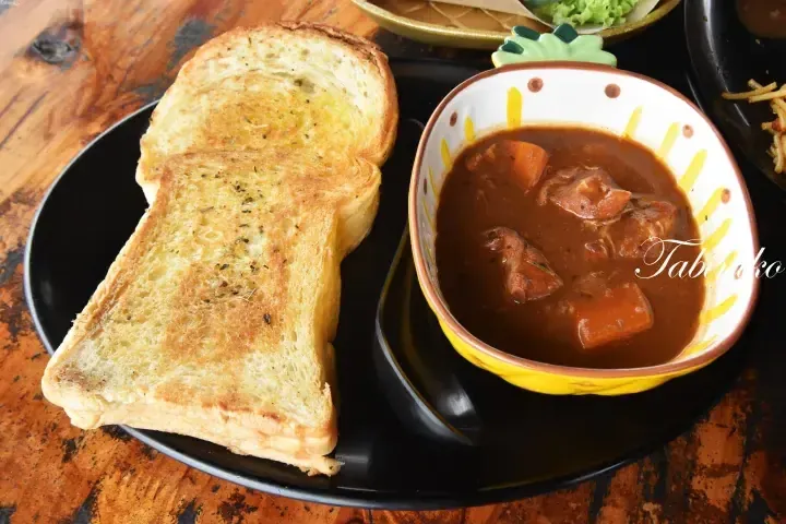 Golden garlic toast served alongside a bowl of hearty beef stew with carrots in a yellow bowl.