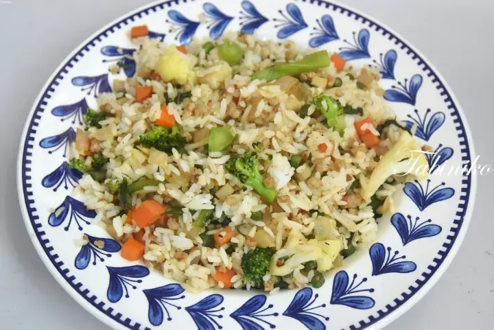 A plate of vegetable fried rice with broccoli, carrots, and pineapple served on a blue and white patterned dish.