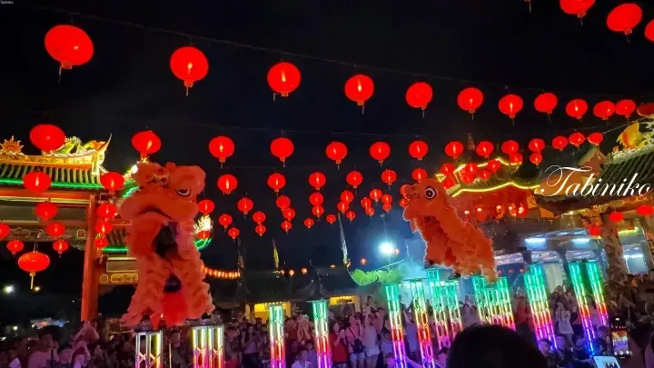 Two lion dancers perform on illuminated platforms under red lanterns at a festive night celebration in Malaysia.