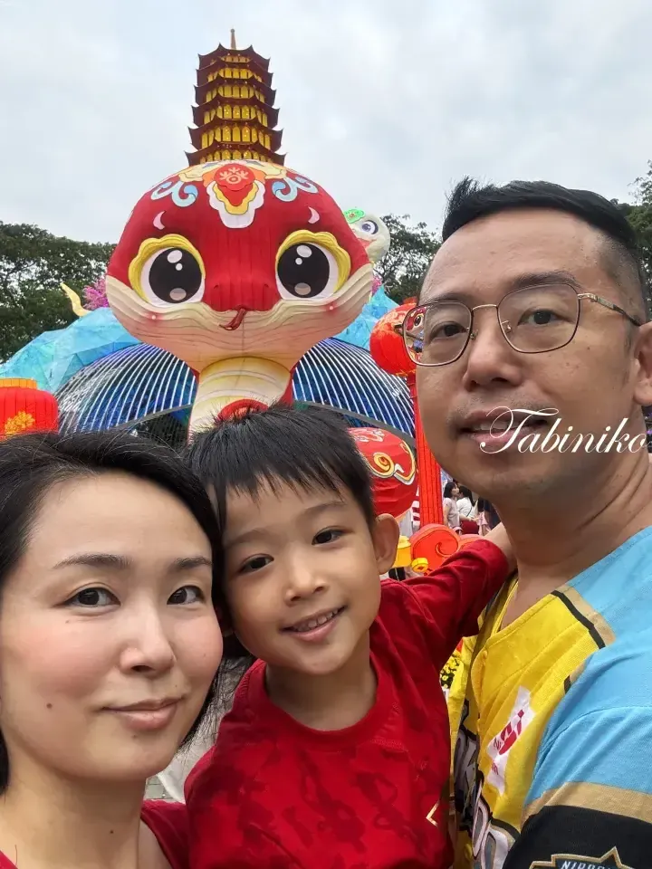 A family selfie in front of a giant red snake lantern and pagoda at the Chinese New Year lantern festival.