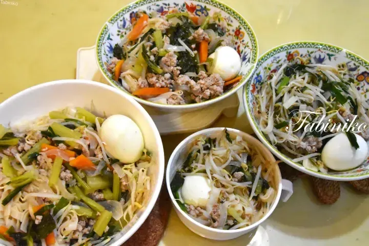 Four bowls of Malaysian mee goreng with minced meat, vegetables, and boiled eggs served on a yellow table.
