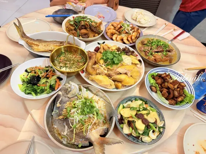 A festive Malaysian family meal featuring steamed fish, roasted chicken, prawns, and stir-fried vegetables on a dining table.