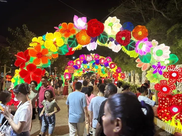 Crowd walking under vibrant floral lantern arches at a night festival in Malaysia.