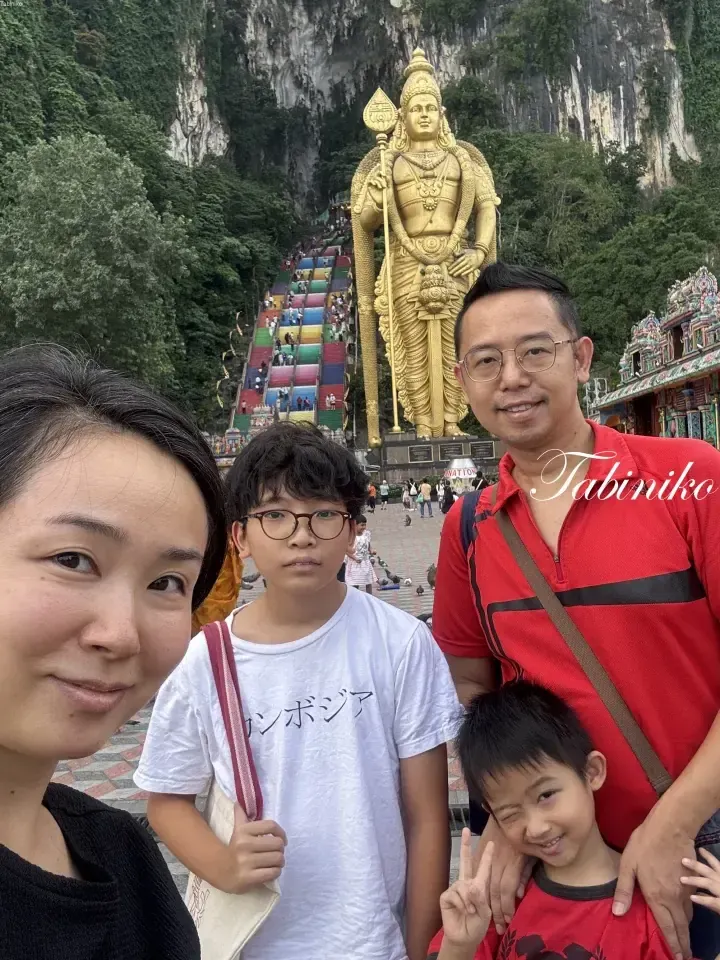 A family poses for a selfie in front of the golden Murugan statue and colorful steps at Batu Caves.