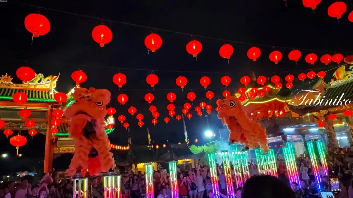 マレーシアの夜祭りで、赤い提灯の下で照明されたプラットフォーム上で獅子舞を披露する2頭の獅子。