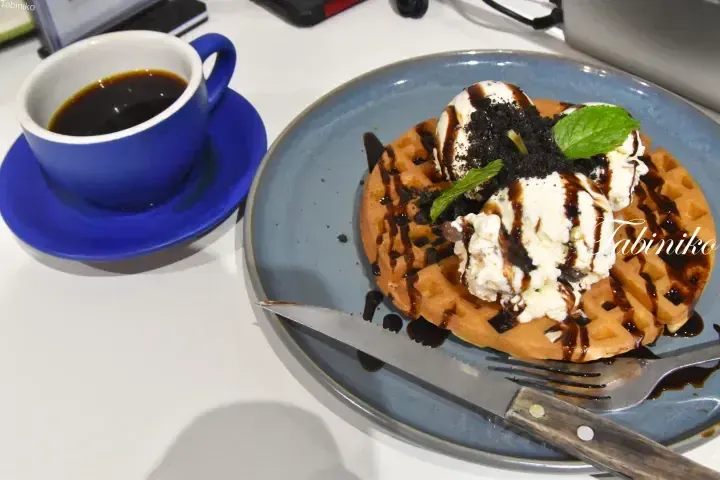 Waffle topped with ice cream, chocolate sauce, and mint served with a blue cup of coffee on a white table