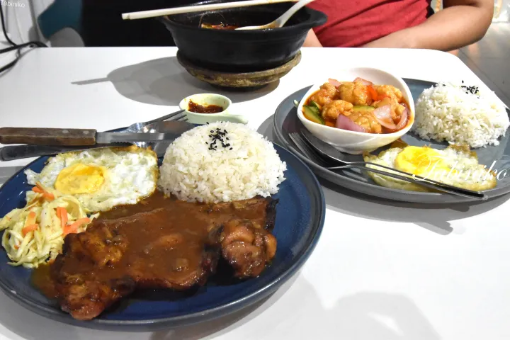 マレーシア料理のライス、フライドエッグ、チキンチャップ、そして甘酢あんかけのチキンが並んだレストランのテーブル。