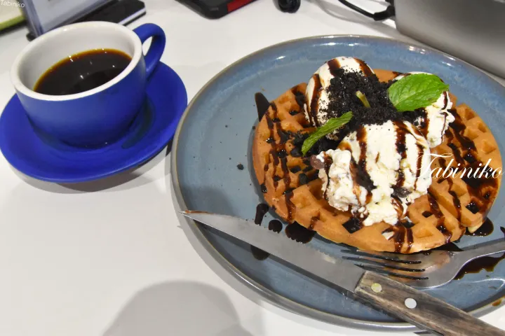 アイスクリーム、チョコレートソース、ミントをトッピングしたワッフルと青いコーヒーカップ
