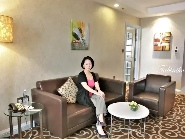 Woman sitting on a brown leather sofa in a hotel suite lounge area with abstract wall art and a glass side table.