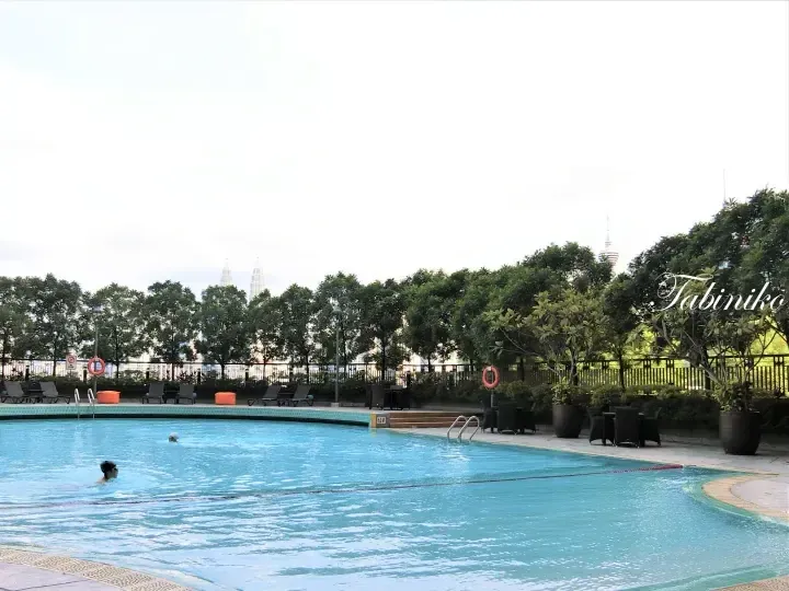 Swimmers in a resort pool with views of the Petronas Twin Towers and KL Tower in the background.