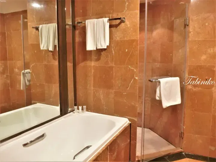 Luxury hotel bathroom with brown marble walls, white bathtub, and glass shower enclosure
