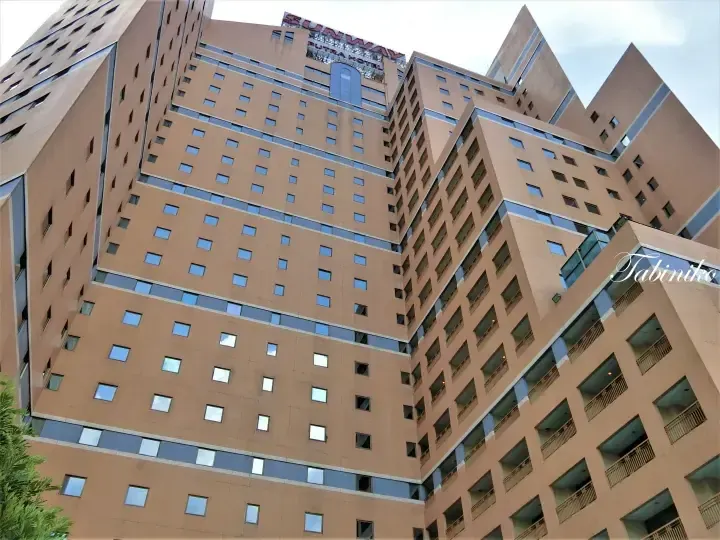 Low-angle view of Sunway Putra Hotel&rsquo;s tall beige facade with rows of windows and balconies against a cloudy sky.