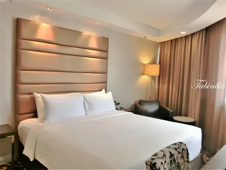Elegant hotel room featuring a large bed with a padded headboard, modern lighting, and a leather armchair.