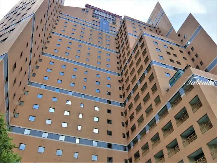 曇り空を背景に、窓とバルコニーが並ぶSunway Putra Hotelのベージュ色の外観を仰視した写真。