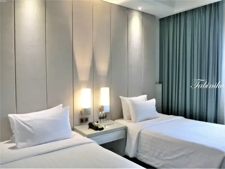 Modern hotel room with two twin beds, white linens, and a nightstand between them.