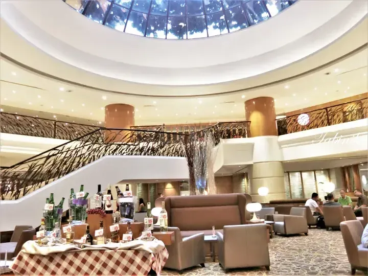 Elegant hotel lobby with spiral staircase, seating area, and wine display under a circular skylight.