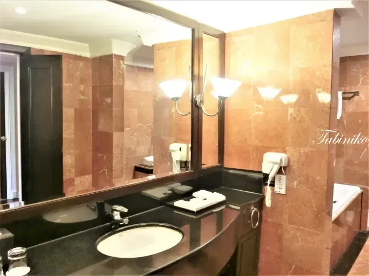Hotel bathroom vanity with black countertop, round sink, large mirror, and brown marble walls.