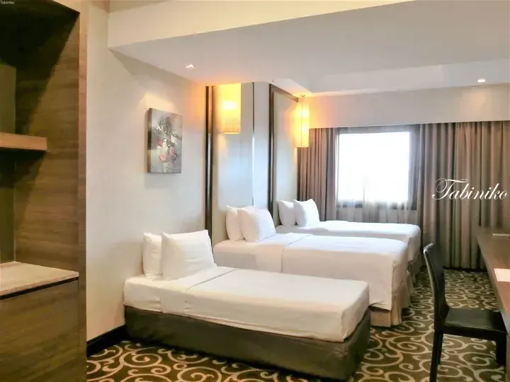Spacious hotel room with three single beds, modern lighting, and a window with curtains.
