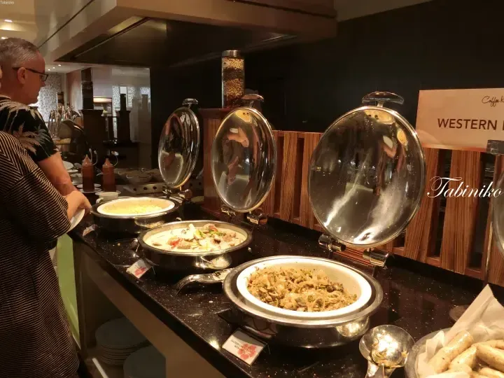 Guests selecting food at a Western buffet station featuring chafing dishes with sauteed chicken liver and other dishes.