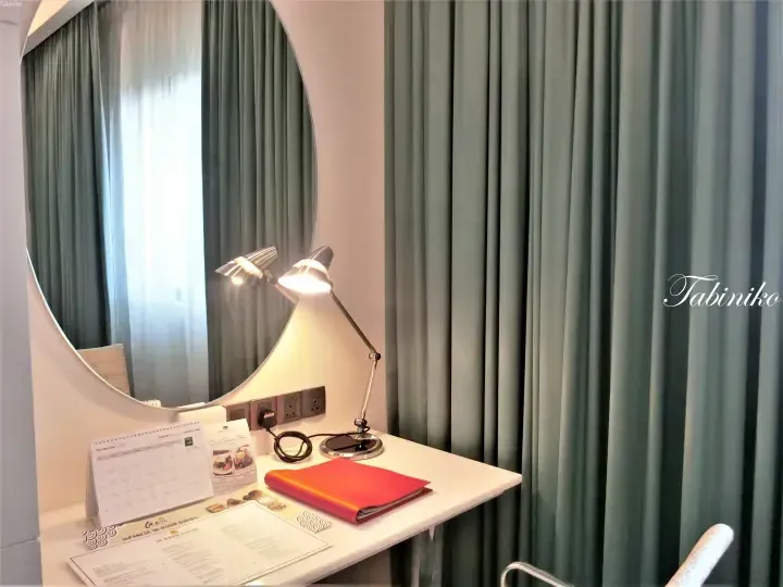 A hotel room desk with a large round mirror, a modern lamp, and a calendar showing November 2019.