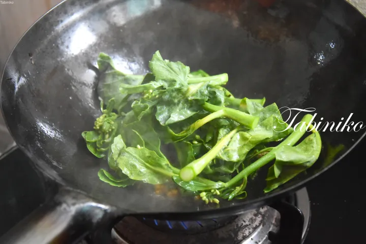 ガスコンロのwokで炒められている新鮮な緑の野菜。