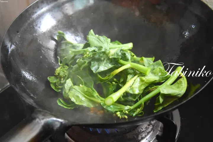 在瓦斯爐上的黑色炒鍋中翻炒的新鮮綠色蔬菜。